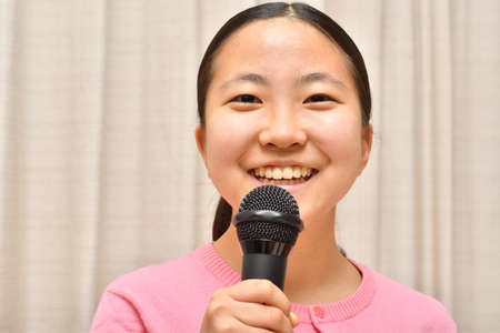 Japanese girl enjoys singing a song by the microphoneの写真素材