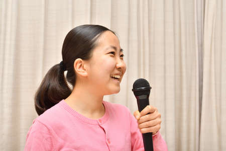 Japanese girl enjoys singing a song by the microphoneの写真素材