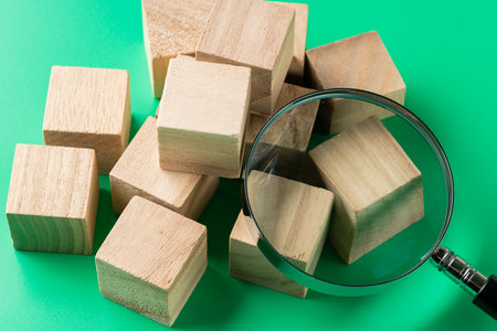 Wooden block cube and magnifying glass on green background