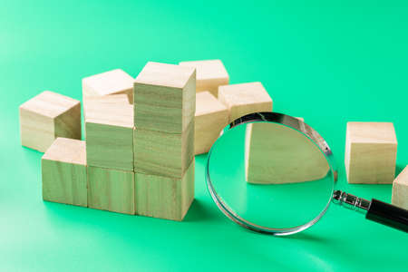 Wooden block cube, graph and magnifying glass on green backgroundの写真素材