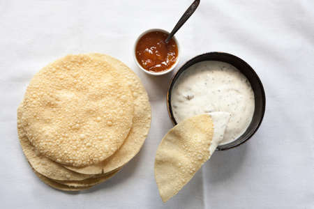 Top view of fresh poppadums and the dishes of raita and mango chutney on the white tablecloth