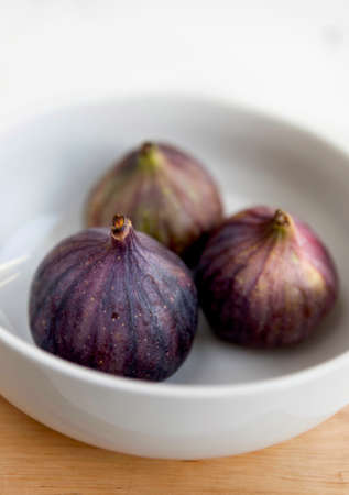 Tree fresh ripe figs in the white ceramic bowl on the white background