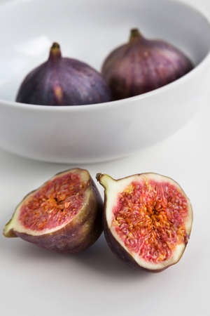 Halved ripe fig on the white table with white ceramic bowl on the backgroundの写真素材