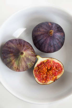 Close-up of tree fresh ripe figs in the white ceramic bowl viewed from above
