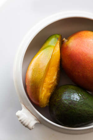 Ripe exotic fruits mangoes and avocado in the white ceramic bowl close-upの写真素材
