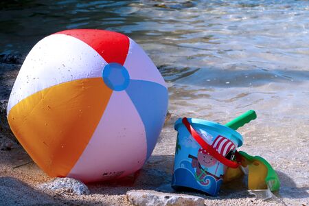 Inflatable beach ball, bucket, shovel and diving goggles on the beach in Italy with sea in the background - summer holiday vacations concept - Italy, Monopoli, Adriatic Seaの写真素材