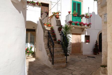 Street in Locorotondo town, Italy, region of Apulia, Adriatic Sea - entrance to the houses with stairway and balcony full of flowersの写真素材