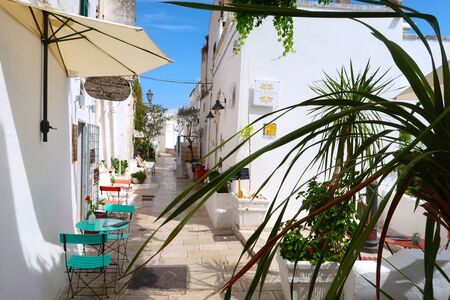 Scenic sight of the Ostuni town sunny street with typical restaurants and blooming flowers, Apulia region, Italy, Adriatic Seaの写真素材