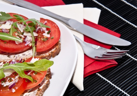 Fresh made tomato bread with onion, cream cheese, rocket salad and Parmesan cheese on a black tablecloth with cutleryの写真素材