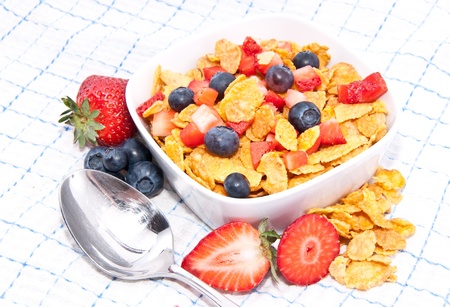 Cornflakes with fruits and a spoon on tablecloth