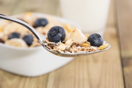 Muesli on a spoon with bowl in the background on woodの写真素材