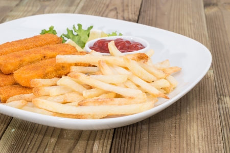 Plate with Chips and Fish Fingers on wooden background