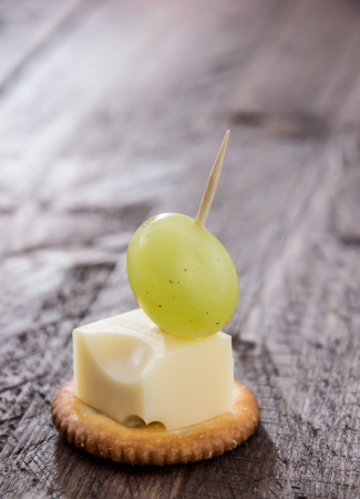 Cracker with a piece of Cheese and a Grape on wooden backgroundの写真素材