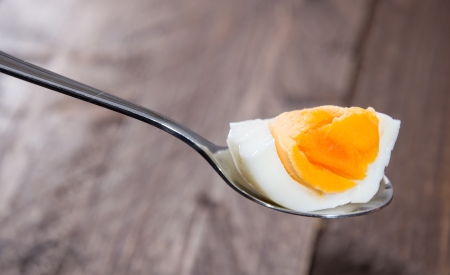 Piece of Egg on a spoon (wooden background)の写真素材