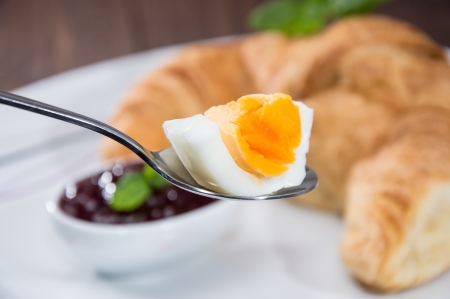 Spoon with piece of egg and croissant in the backgroundの写真素材