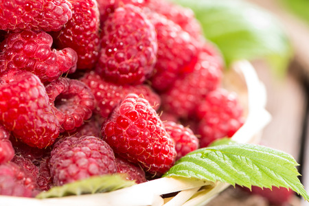 Small basket with fresh harvested Raspberries on wooden background
