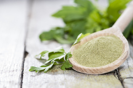 Lovage Powder on a wooden spoon with some fresh green leavesの写真素材