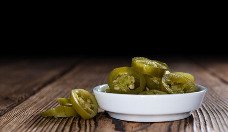 Portion of preserved Jalapenos (close-up shot) on wooden background