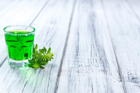 Woodruff Liqueur in a small shot glass (on wooden background) Woodruff Liqueur in a small shot glass (on wooden background)