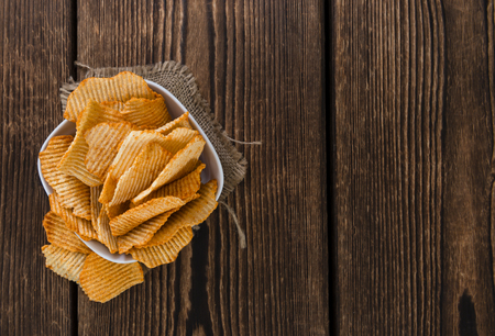 Portion of rippled Potato Chips (selective focus) on an old wooden tableの写真素材