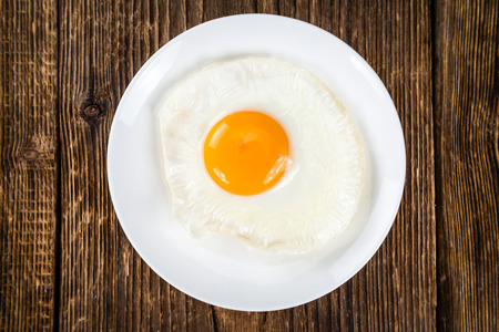 Breakfast (fried eggs) on an old wooden table (selective focus; close-up shot)