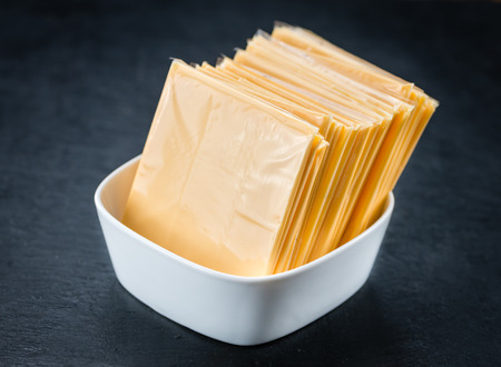 Portion of Cheese slices on a rustic slate slab (selective focus; close-up shot)