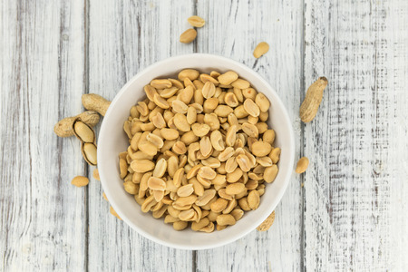 Old wooden table with salted and roasted peanuts (close-up shot; selective focus)
