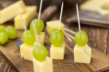 Vintage wooden table with Cheese blocks and grapes as detailed close-up shot (partyfood)の写真素材