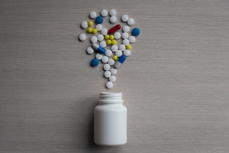Assorted pharmaceutical medicine pills, tablets and capsules and bottle on blue background