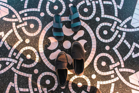 A pair of sandals and shoes in the middle of a Mandala tiles on a floor shone by the evening sunの写真素材