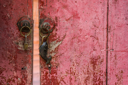 Aged wooden red door with moden and rusty vintage style fish shape padlocksの写真素材