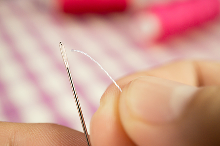 Hand being to push white thread pass hole of sewing needle, close up picture