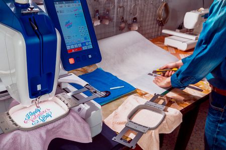Working scene of the embroidery, worker cutting light cutaway backing use on towel and machine...