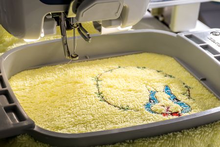Close up image of workspace embroidery machine embroidering cartoon rabbit on yellow towelの写真素材
