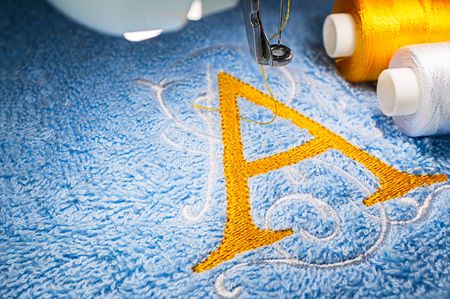 Macro image of yellow alphabet design on blue towel and two threads in hoop of embroidery machineの写真素材