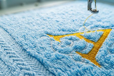 Close up picture embroidery design yellow alphabet monograme on blue towel embroider by machine, copy space on the left side.の写真素材