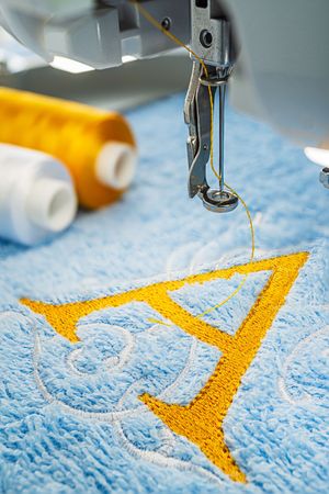 Embroidery machine and yellow alphabet logo design on blue towel in hoop and two threads, close up imageの写真素材