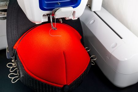 Close up picture of black and red cap on the hoop of white embroidery machine ready to embroidering.