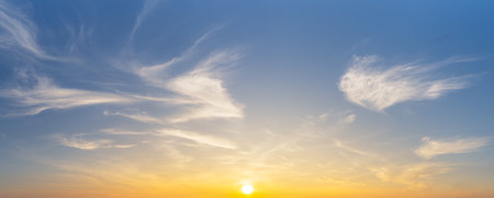The yellow sun and white smooth cirrus clouds on blue sky, nature sunrise panorama background.の写真素材