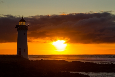 Port Fairy lighthouse beach with red glowing sunrise in background.の写真素材