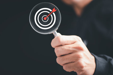 Man hold Target board inside of magnifier glass for focus business objective achievement concept on blue background and copy space. Search, goal, strategy, success.の写真素材