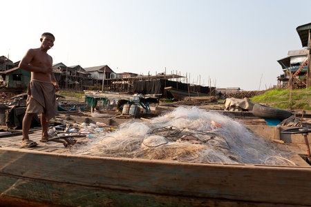 Floating village of Kom Pong Pluke, Siem Reap, Cambodia. February, 3rd, 2011. A fisher man is standing on his boat with a pile of fishing net. The whole village is built over the water and is very poor fishing village. のeditorial素材