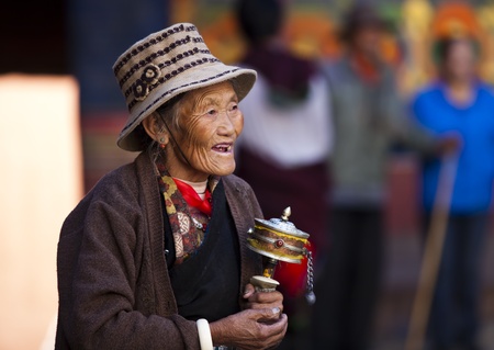 Lhasa, Tibet, China - October 05, 2011: a senior female Tibetan prayer holding a prayer wheel at monastery.のeditorial素材