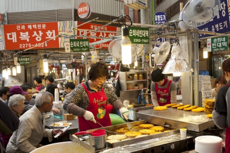 Seoul, South Korea - April 27, 2013: A female vendor is cooking traditional Korean pie for customers at the Gwangjang Market which is the nation