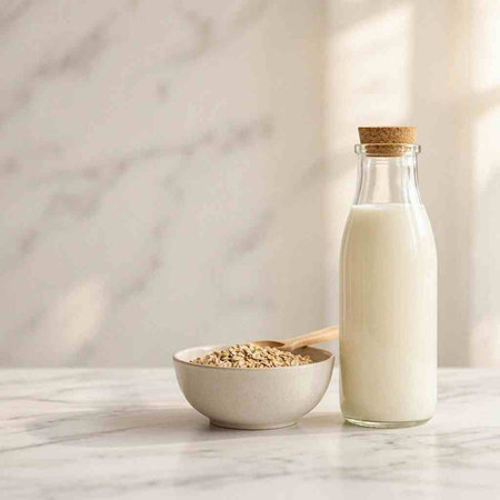 Oat milk in a glass bottle and a bowl with oatmeal on a white marble table.