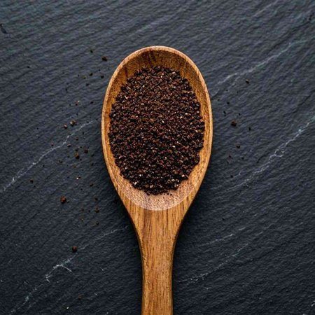 Black pepper in a wooden spoon on a black background. Top view.