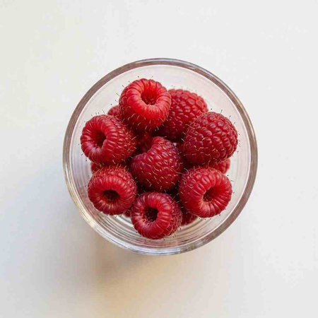 Raspberries in a glass bowl on a white background, top view