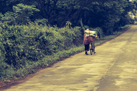 Older women walking bicycle trailer with many baggage along the road, which has no destination - vintage style.の写真素材