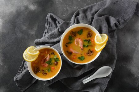 Tom Yam - traditional spicy Thai soup with shrimps,coconut milk, chilli pepper, lemon, mushrooms. Asian soup. White bowls on dark background.の写真素材