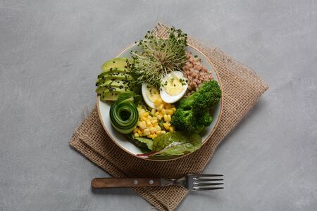 Green vegetarian Buddha bowl lunch with boiled egg, avocado, corn, arugula beet leaves,fresh cucumber, buckwheat, broccoli sprouts.Healthy vegan food conceptの写真素材